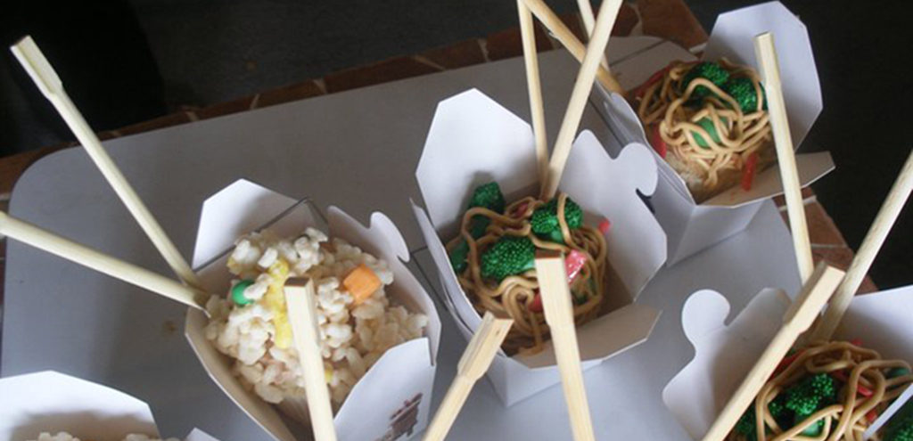 cupcakes with faux-takeput toppings placed inside takeout cartons with chopsticks